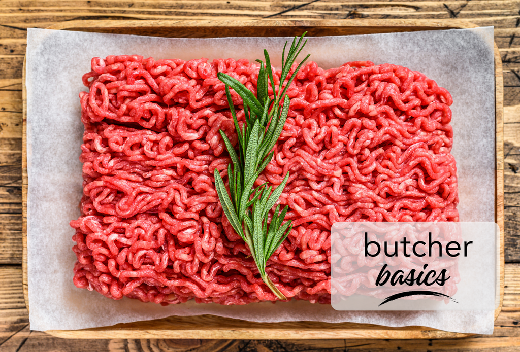 A mound of fresh ground beef topped with thyme on white parchment paper laying in a wooden serving tray