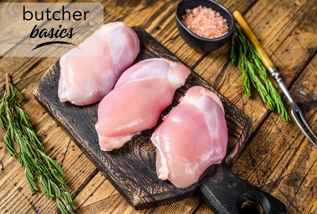 Three air-chilled boneless, skinless chicken thighs displayed with fresh thyme and garlic bulbs on a dark, wooden cutting board