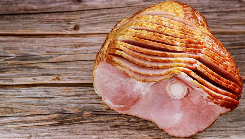 Sliced glazed spiral ham on a wooden board background