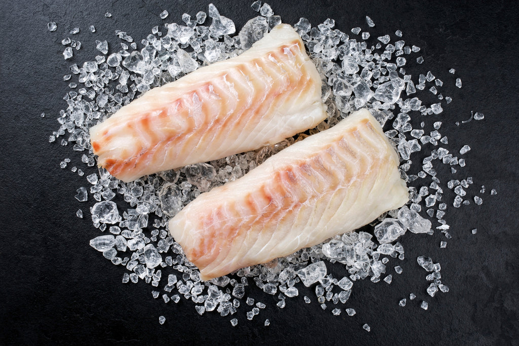 two filets of fresh cod loins, on ice chips, sitting on a black slate board