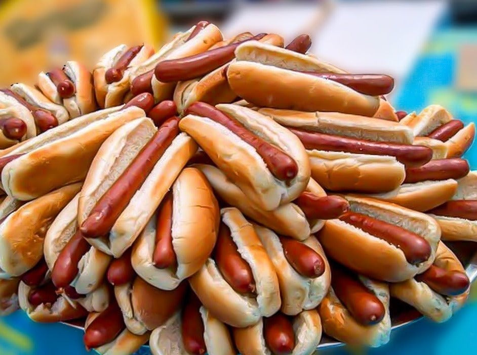 A heaping pile of Nathan’s franks in hot dog buns on a silver serving tray against a blurred background