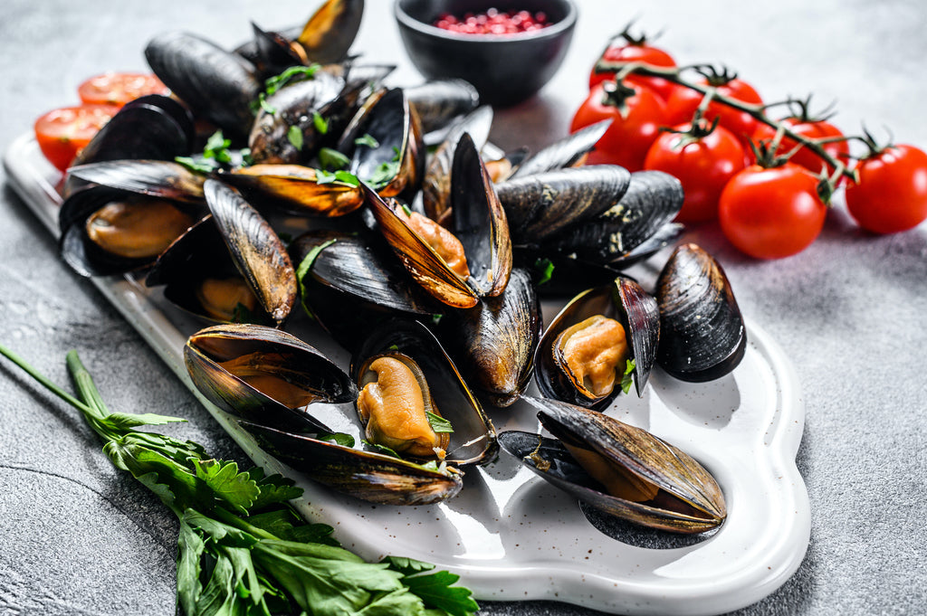steamed mussels on a white serving platter, garnished with herbs and tomatoes