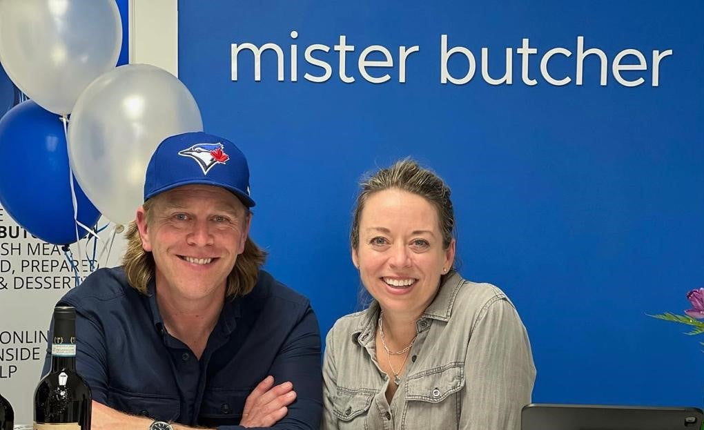 Mister butcher founders – Jonathan and Christine – with balloons and “mister butcher” sign on a blue background