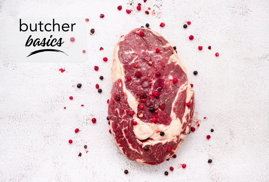 A single, fresh ribeye steak sprinkled with coloured peppercorns on a white background