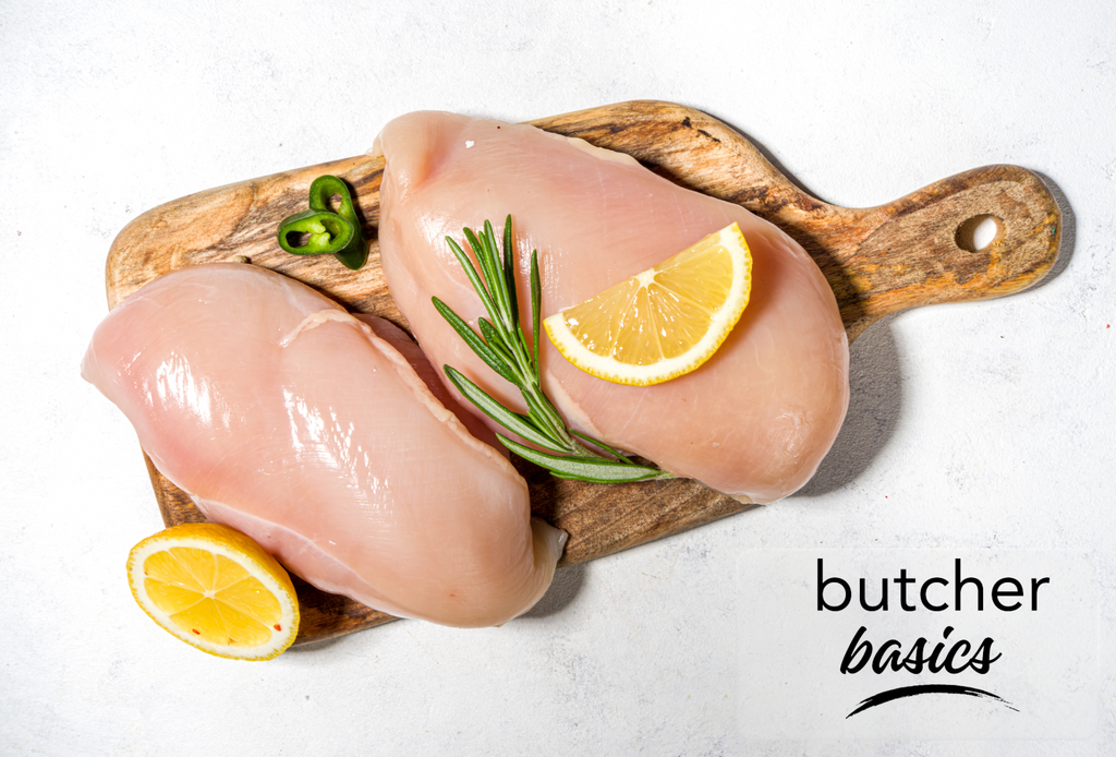 Two air-chilled boneless, skinless chicken breasts displayed with fresh thyme and lemon wedges on a wooden cutting board 