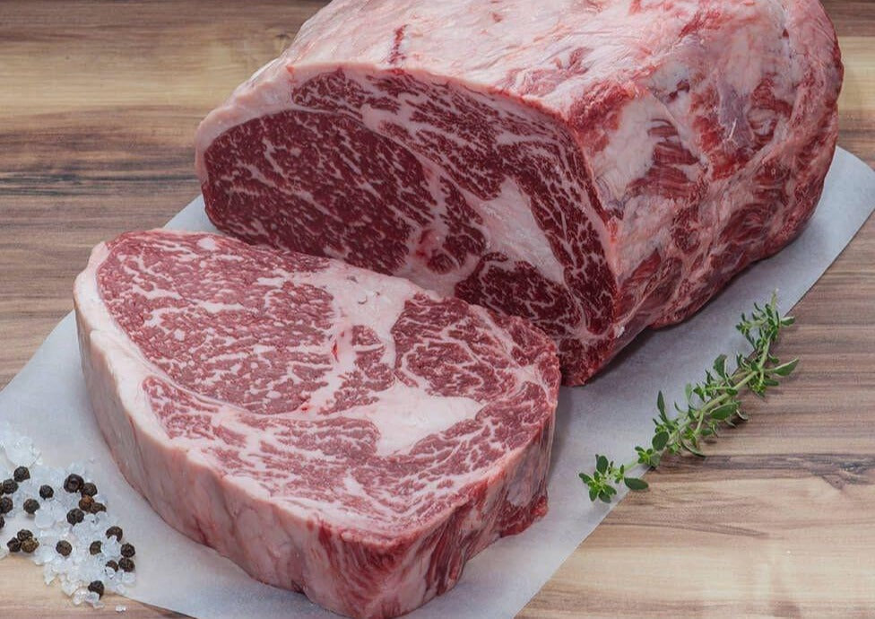 A sliced slab of Tajima Australian Wagyu Ribeye steak surrounded by peppercorns and thyme on white parchment paper