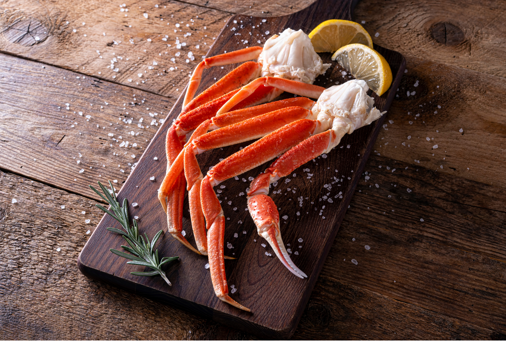 Snow Crab clusters with rosemary and lemon wedges sprinkled in sea salt on a dark brown cutting board