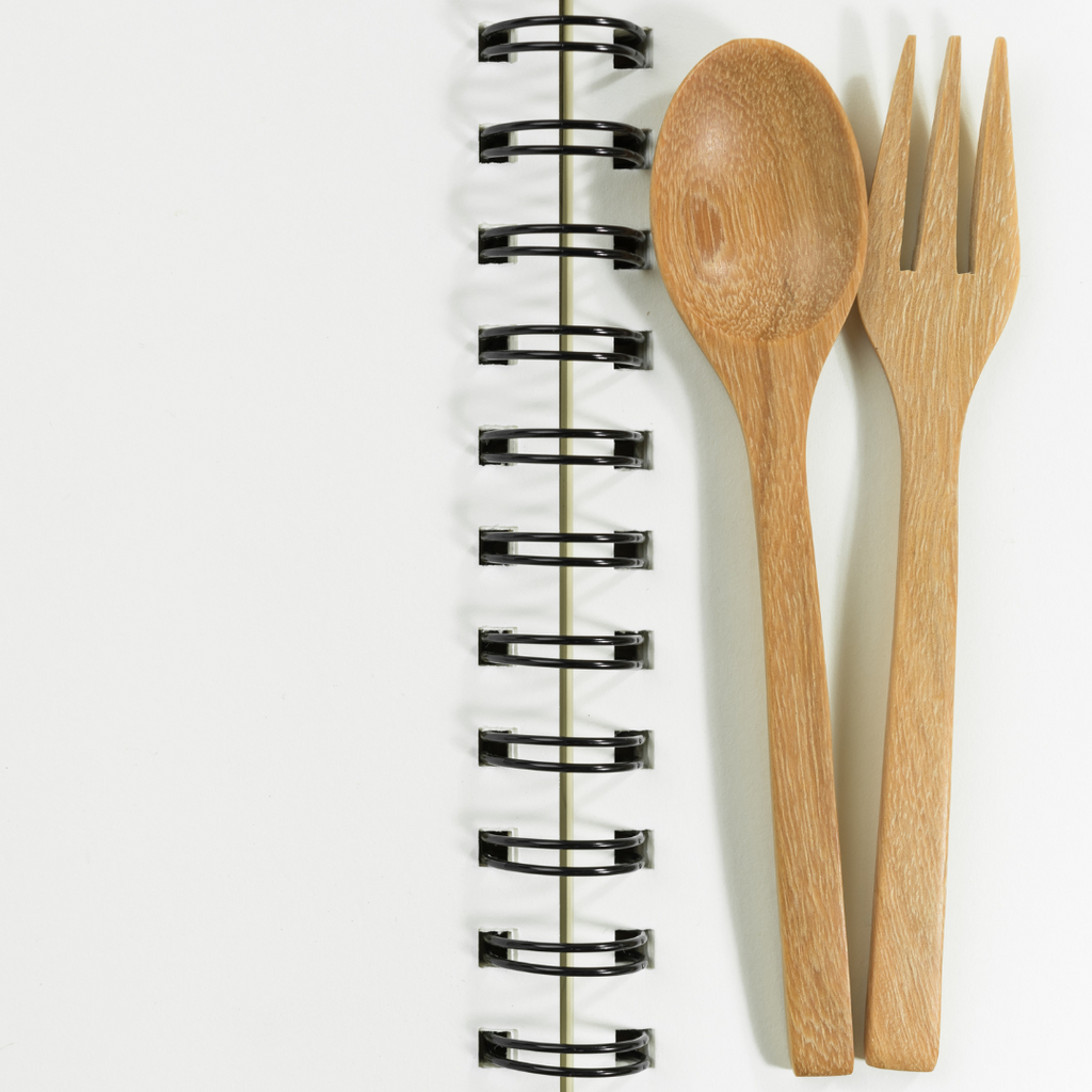Wooden spoon and fork lying beside binding rings of a recipe book