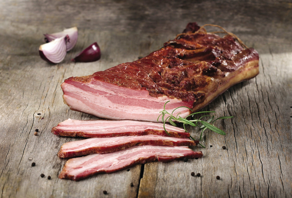 slab of bacon with three pieces sliced, sitting on a wooden board