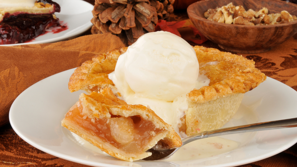 A fresh slice of apple pie with a dollop of vanilla ice cream on a white plate