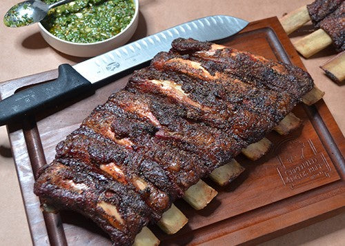 Cooked beef ribs with butcher knife on a brown cutting board