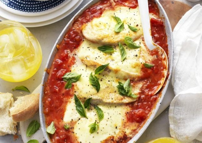 Cooked chicken parmigiana with white spoon in porcelain serving dish