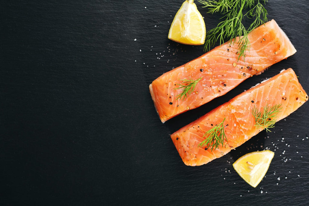 Two scaled salmon portions with lemon wedges and rosemary against a black background