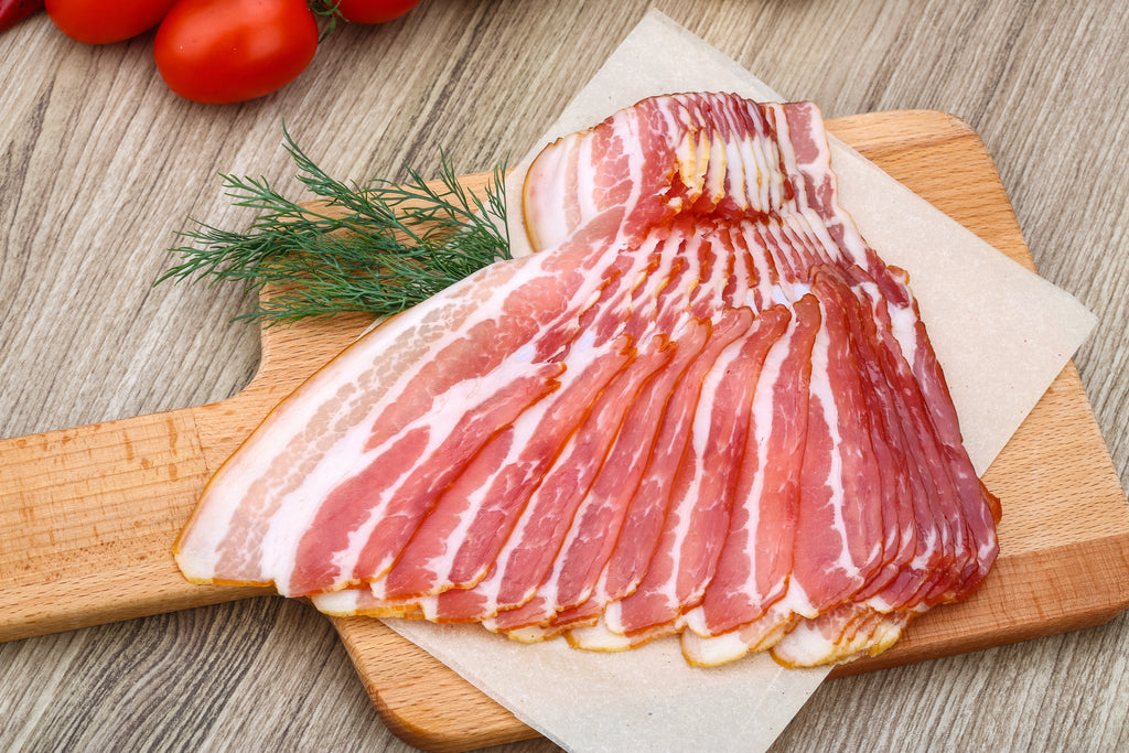 bacon slices fanned out on parchment paper, on a wooden board with roma tomatoes in the background