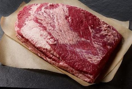 Fresh beef brisket on brown butcher paper against a black background
