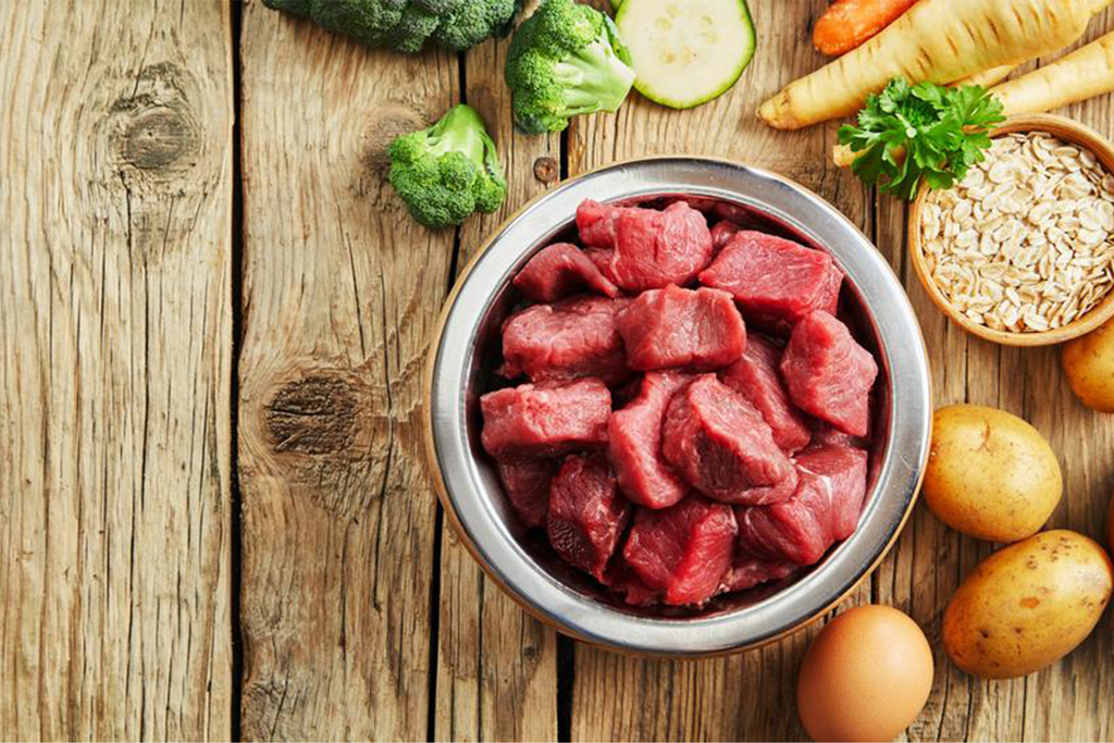 bite sized pieces of uncooked beef in a bowl, surrounded by vegetables