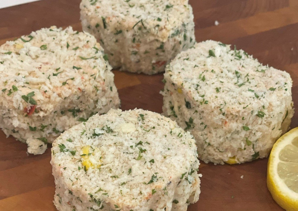Four uncooked seasoned crab cakes with a slice of lemon on wooden cutting board