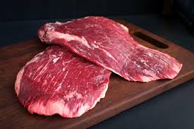 Two portions of fresh flank steak on a brown cutting board with a black background