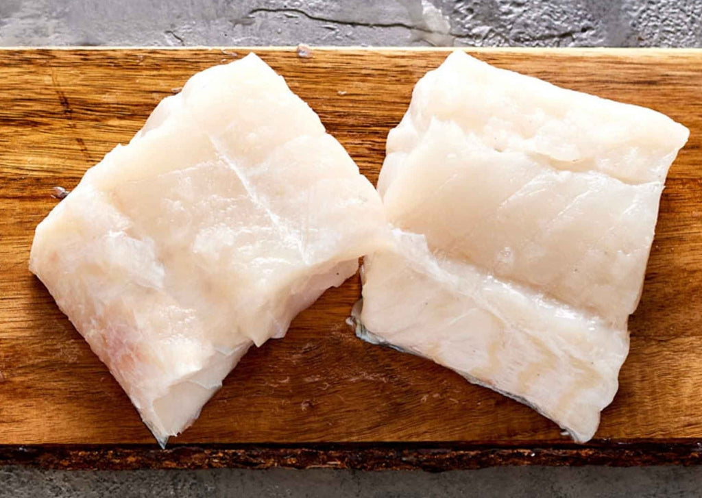 Two fresh cod fillets on a wooden cutting board
