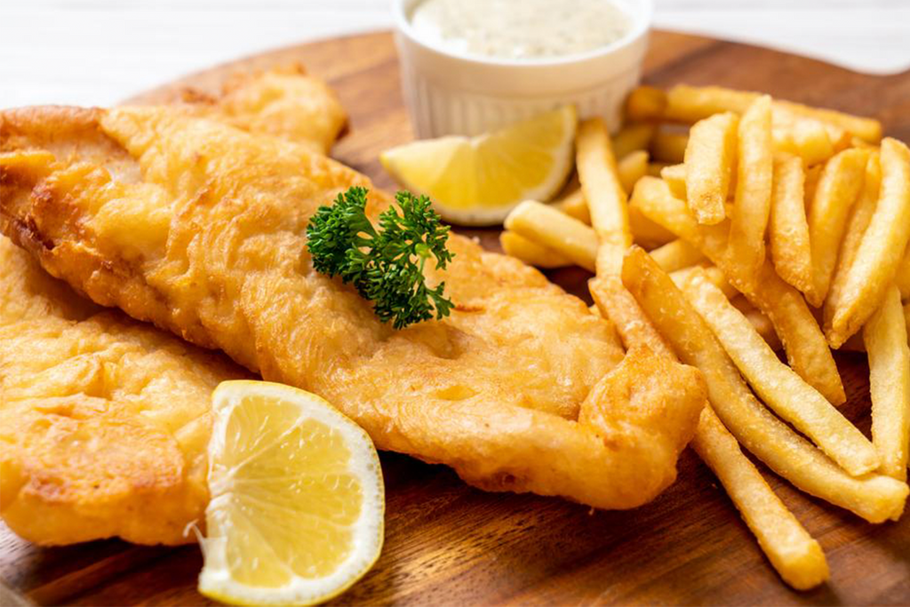 two pieces of battered fish next to french fries, fish and chips, with lemon on a wooden board