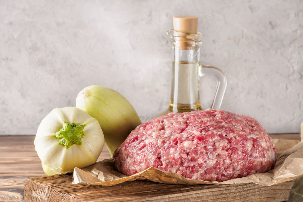 Ground sausage meat on parchment paper with olive oil and onions on a wooden cutting board
