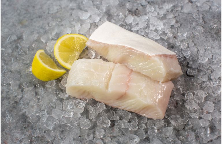 Two fresh skin-on halibut fillets with lemon wedges on a bed of ice