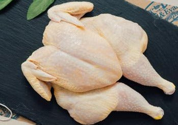 A fresh, whole, flattened chicken on a black wooden cutting board