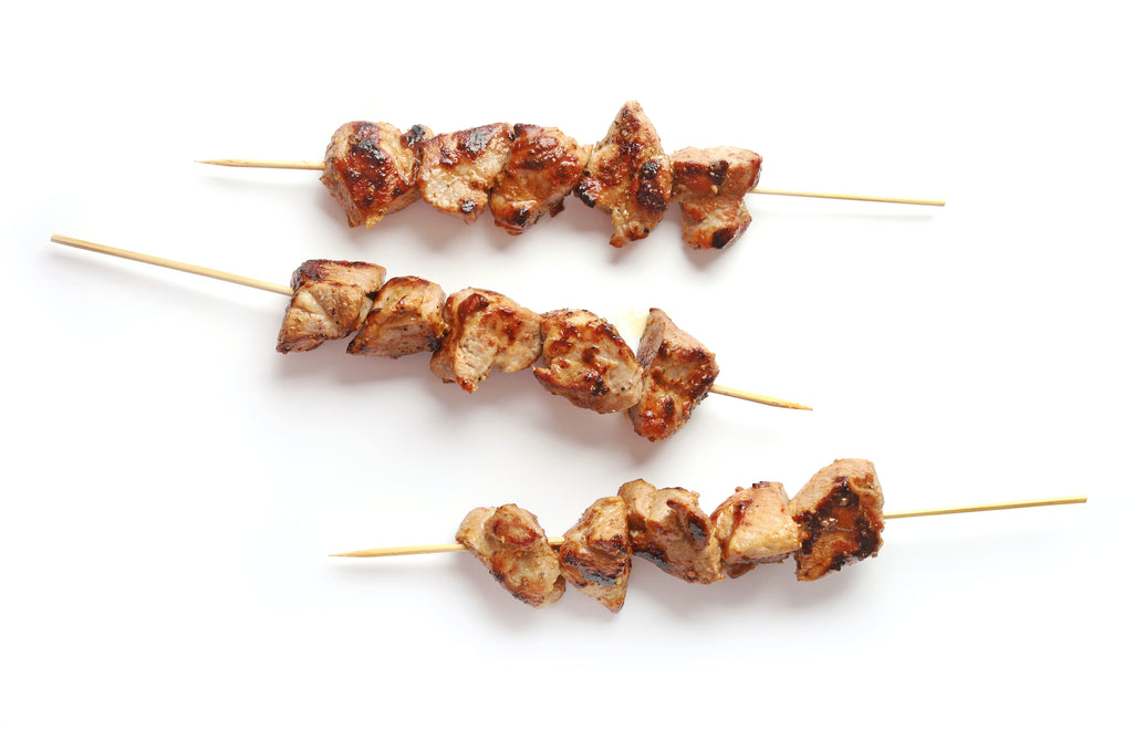 three grilled pork kabobs on wooden skewers on a white background