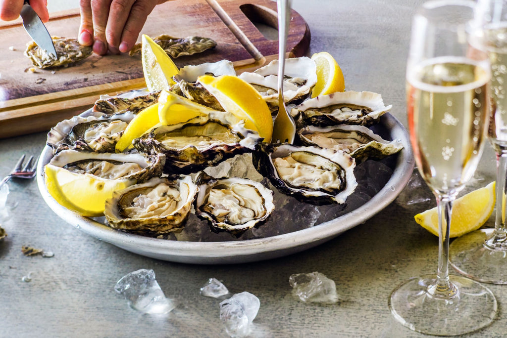 Oysters and lemon wedges on a plate beside a glass on white wine