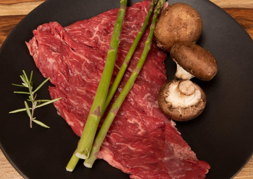 Fresh uncooked bavette steak with rosemary, mushrooms and asparagus on a black plate