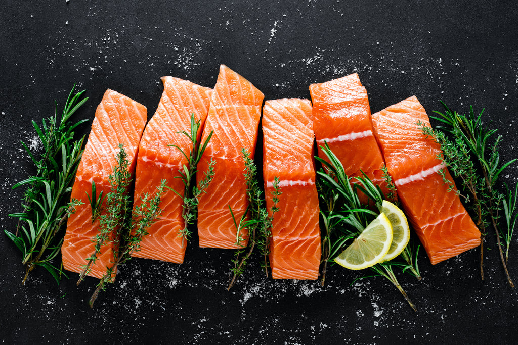 Six fresh salmon pieces with rosemary and lemon slices on a black background