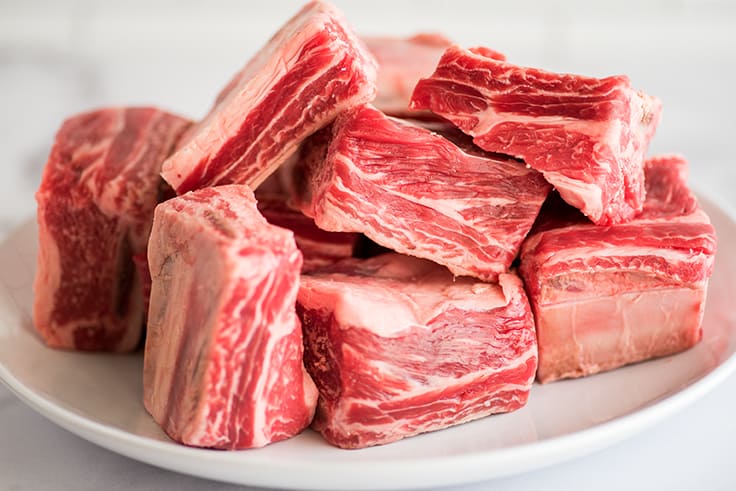 fresh beef short ribs piled on a white plate
