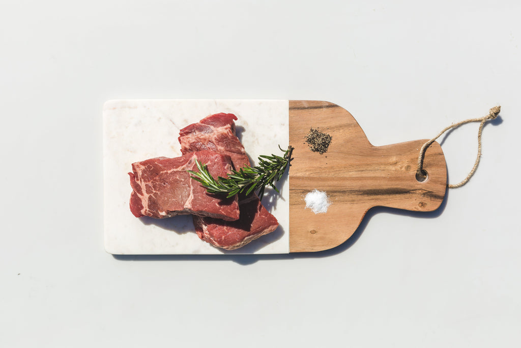 three steaks ready to be seasoned and grilled, on a white and wooden board