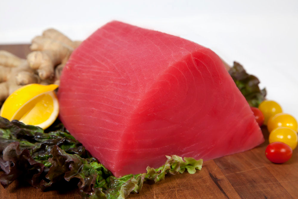 Fresh tuna loin surrounded by lemon wedges, lettuce and cherry tomatoes