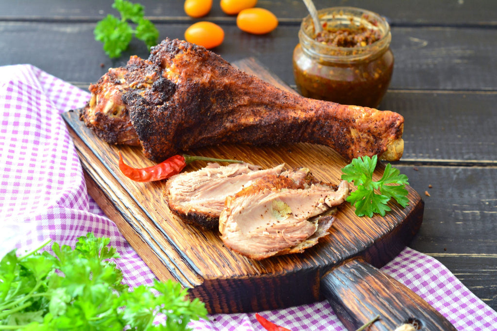 Cooked turkey leg and garnishes served on a wooden cutting board surrounded by a purple and white table cloth 
