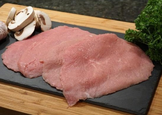 Four thinly-sliced portions of veal scallopini and mushrooms on a black slate cutting board
